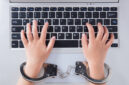 Child's hands in handcuffs with laptop in the office