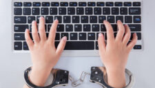 Child's hands in handcuffs with laptop in the office