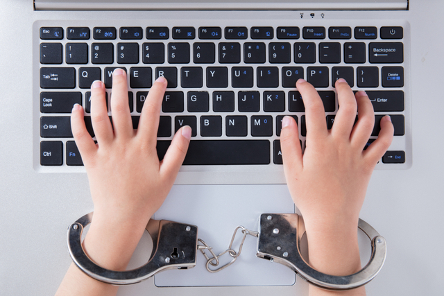 Child's hands in handcuffs with laptop in the office